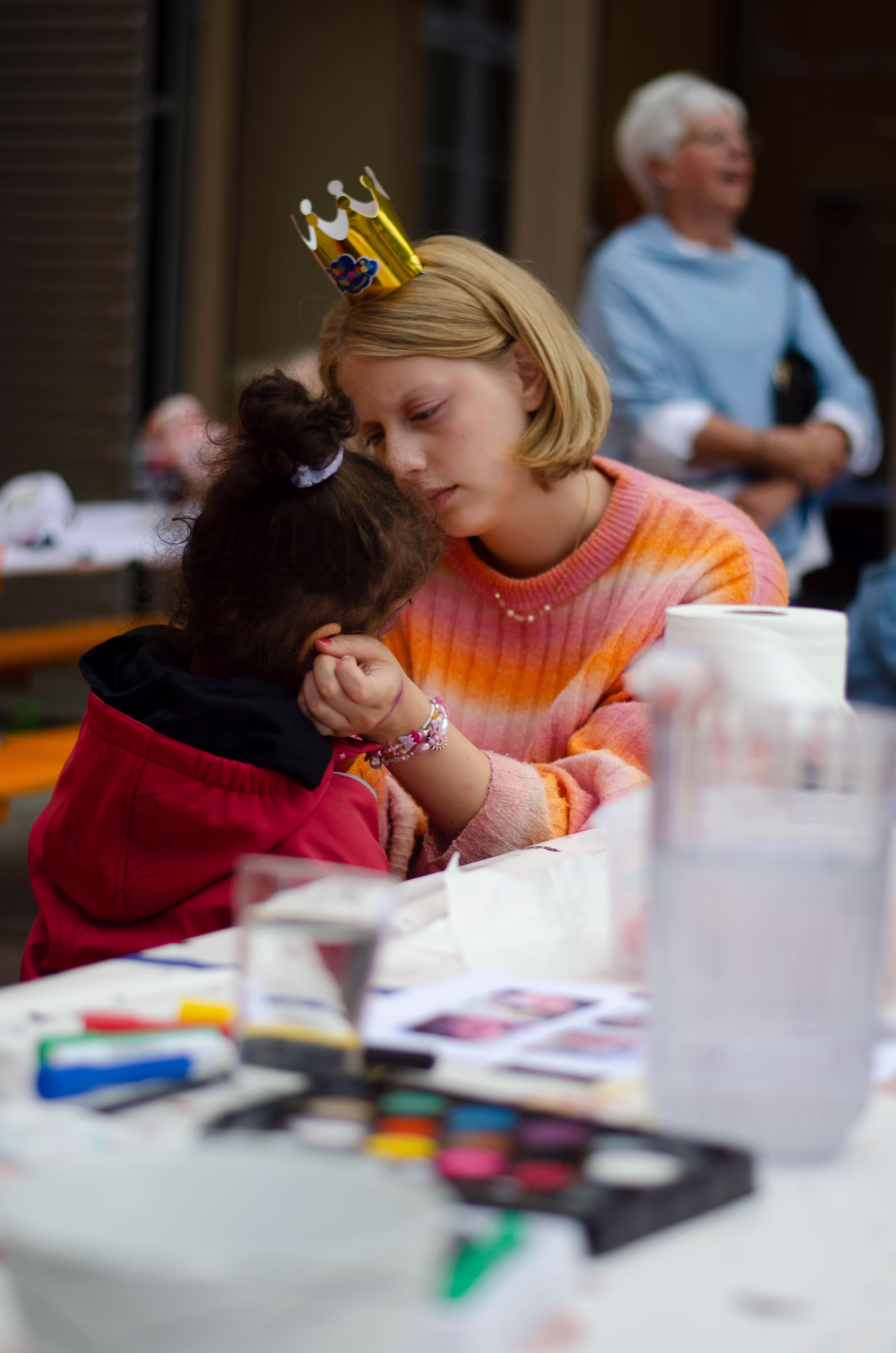 Et barn sitter med ryggen til og blir ansiktsmalt av en frivillig.