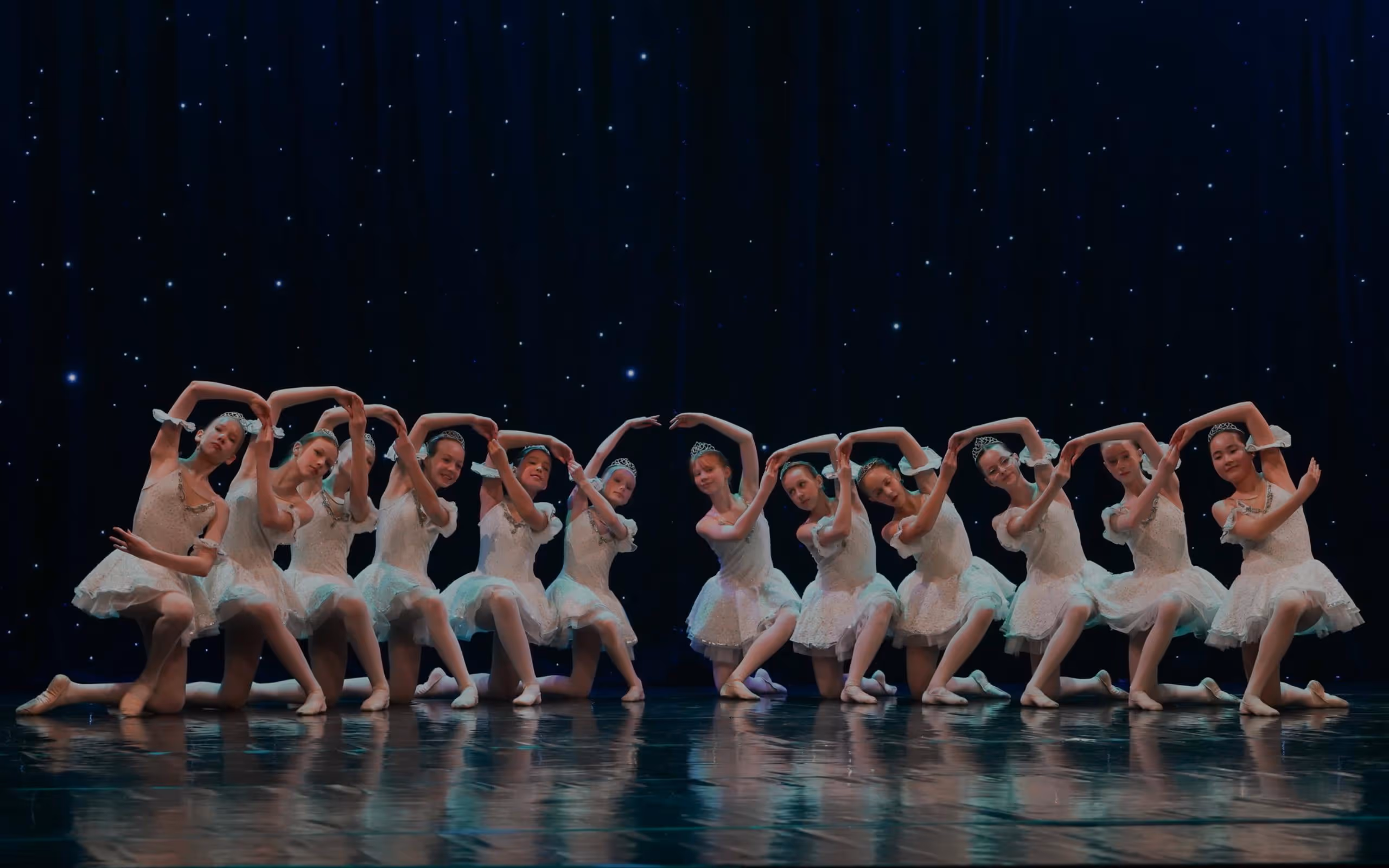 mange ballerinaer står i en vakker konstruksjon foran et sort teppe