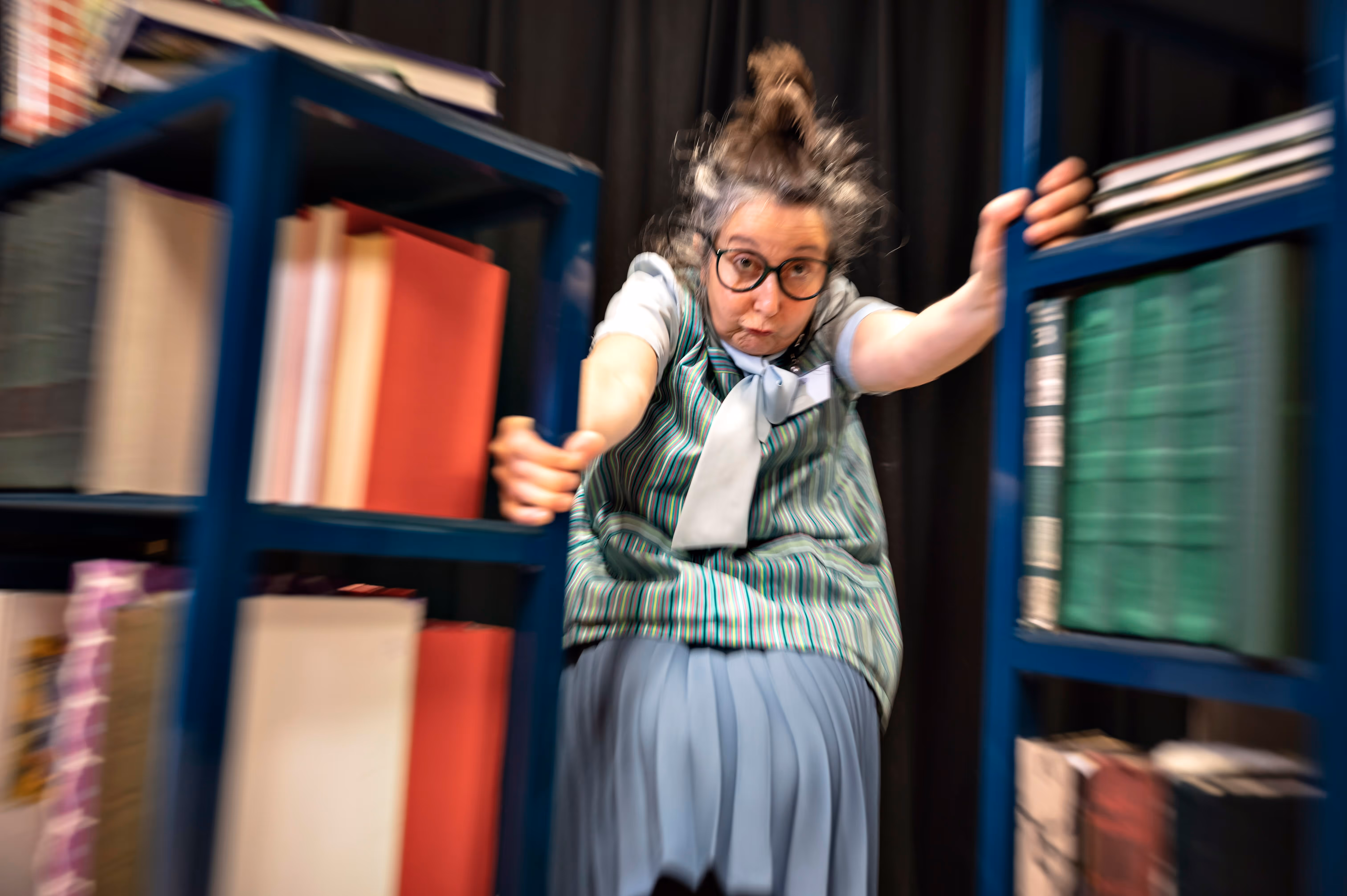 en eldre dame blir kastet bak forbi 2 bokhyller. Bildet har motion blur