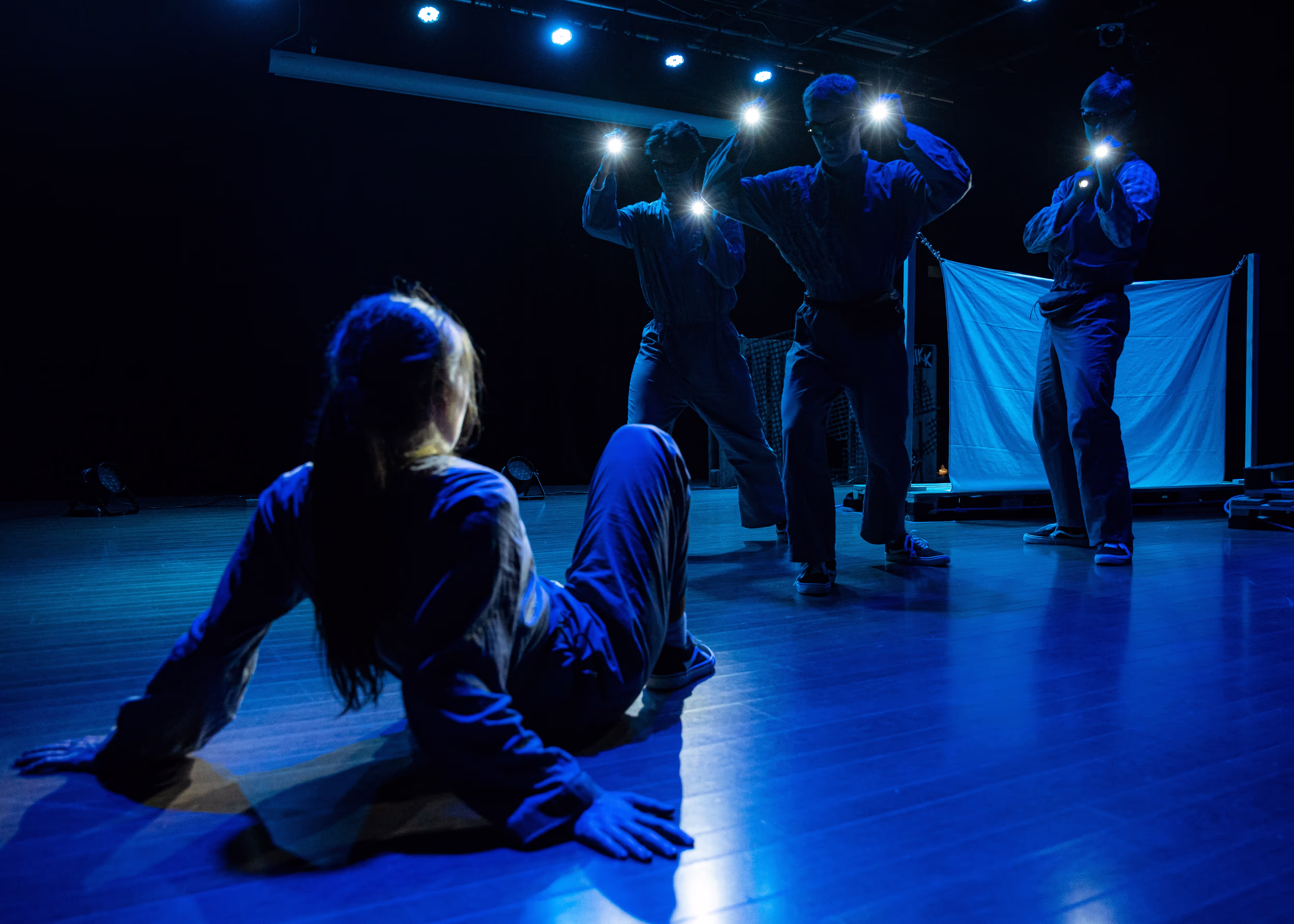 Et bilde fra forestillingen Det Grønne Skiftet. Ei jente ligger på bakken mens tre skumle skikkelser står over henne med lommelykter.