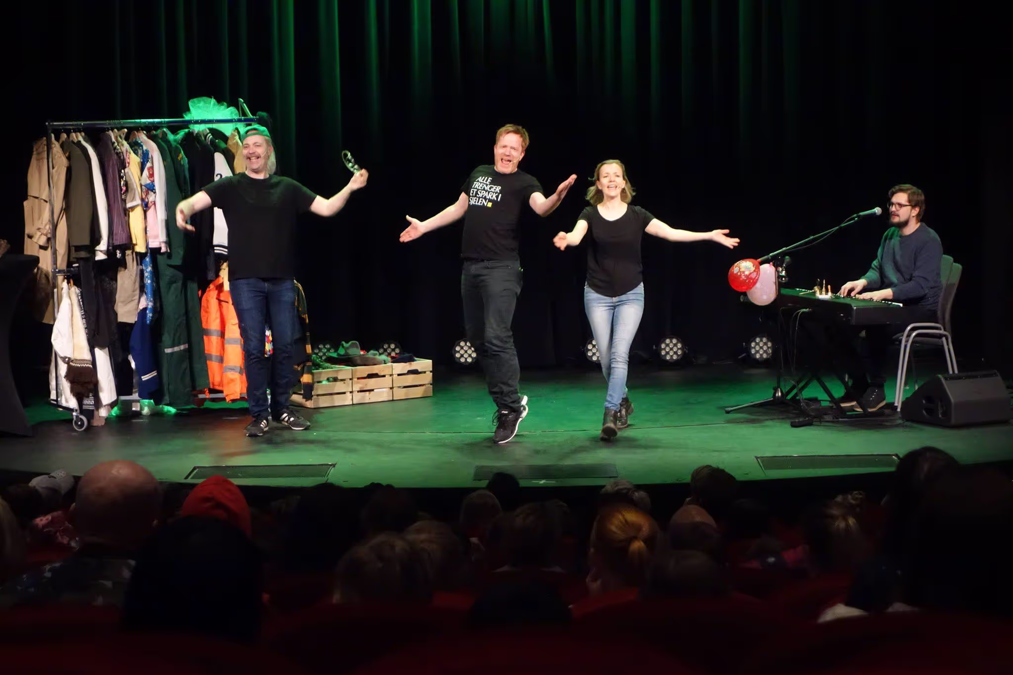 Et bilde fra forestillingen Plutselig Barneteater. To mennesker står foran på en scene, mens en musiker sitter bak et piano.